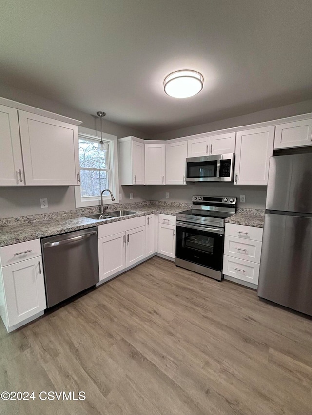 kitchen featuring white cabinetry, sink, stainless steel appliances, pendant lighting, and light hardwood / wood-style floors