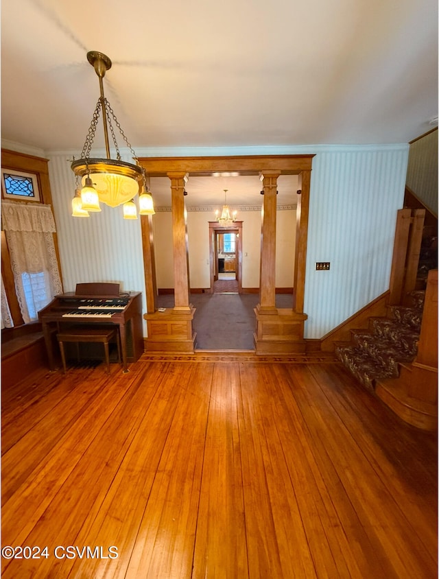 unfurnished living room with hardwood / wood-style floors, ornate columns, and a notable chandelier