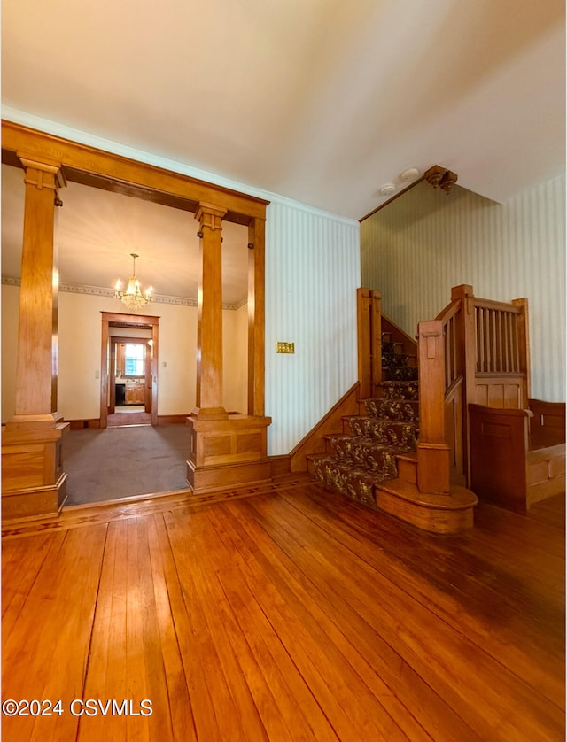 interior space featuring hardwood / wood-style flooring, crown molding, decorative columns, and a notable chandelier