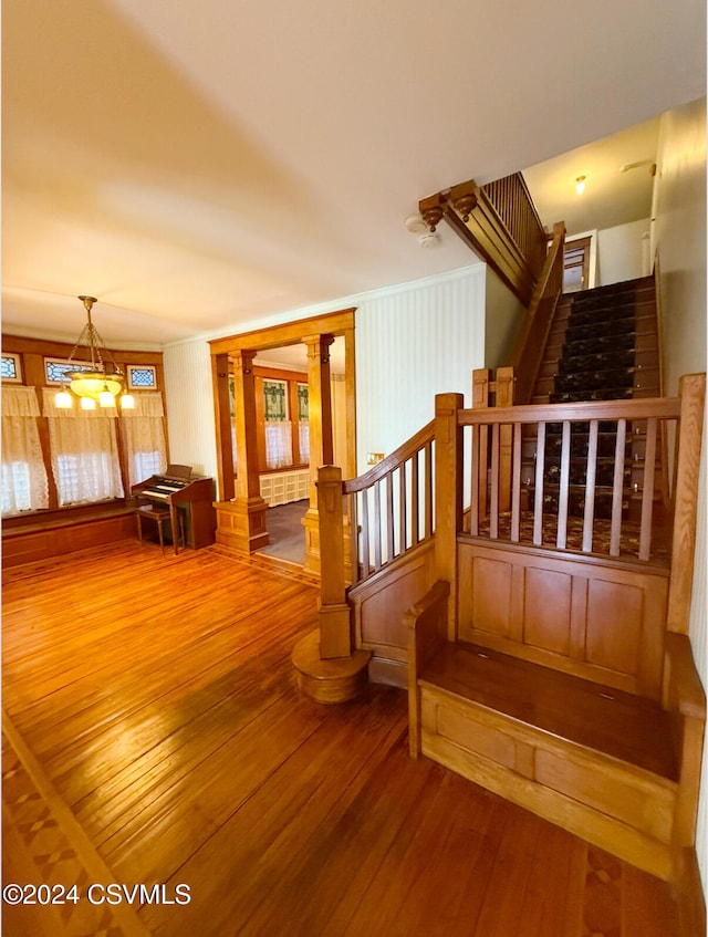 stairs with crown molding, hardwood / wood-style flooring, a notable chandelier, radiator heating unit, and decorative columns