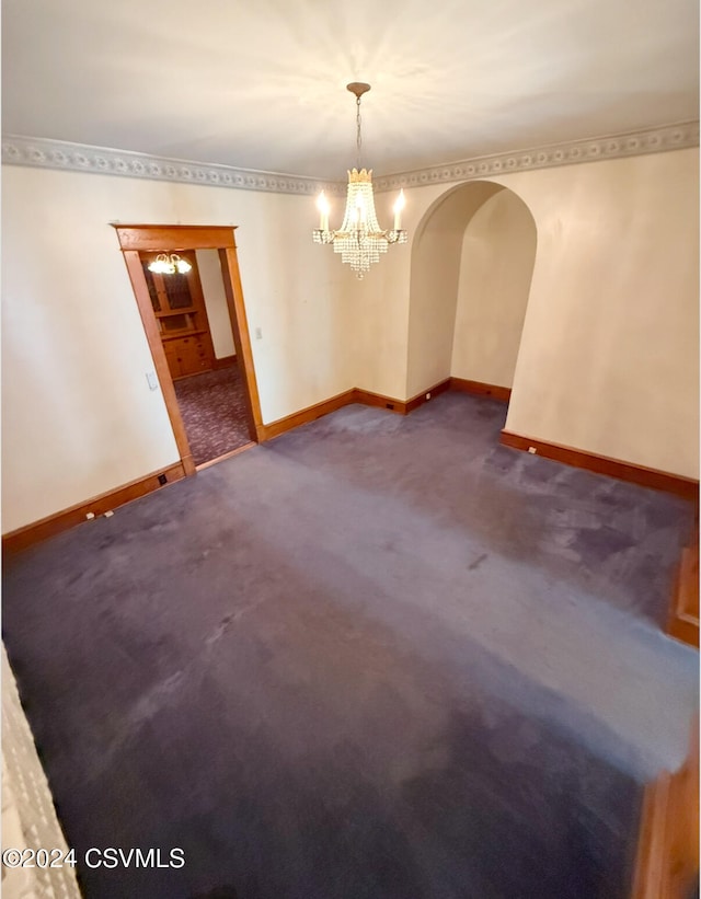 empty room with dark colored carpet and an inviting chandelier