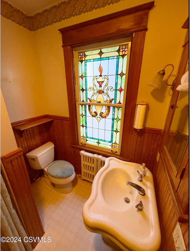 bathroom with radiator heating unit, sink, toilet, and wood walls