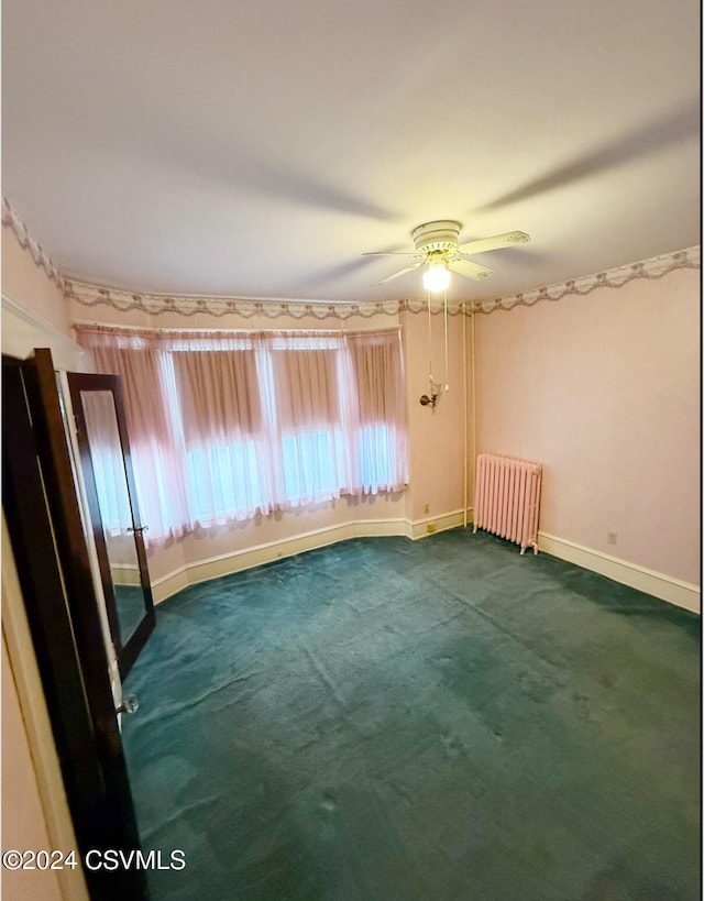 unfurnished room featuring radiator heating unit, dark carpet, and ceiling fan