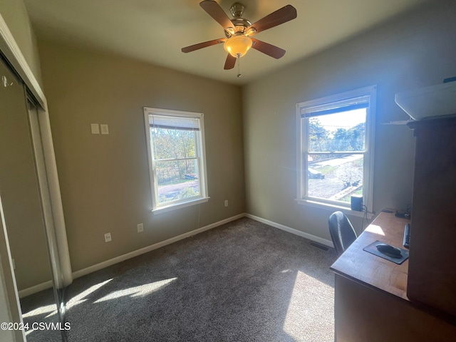 unfurnished office with dark colored carpet, a wealth of natural light, and ceiling fan