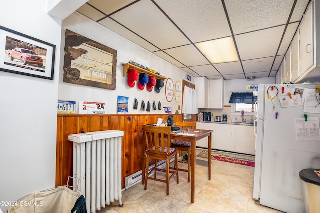 kitchen with radiator heating unit, sink, a drop ceiling, white refrigerator, and white cabinets