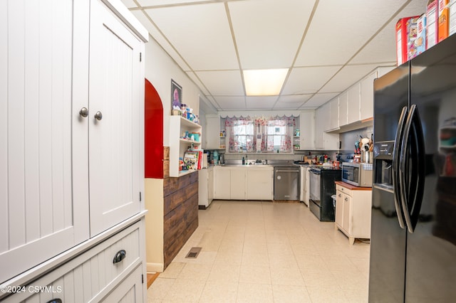 kitchen with black appliances, a drop ceiling, white cabinetry, and sink