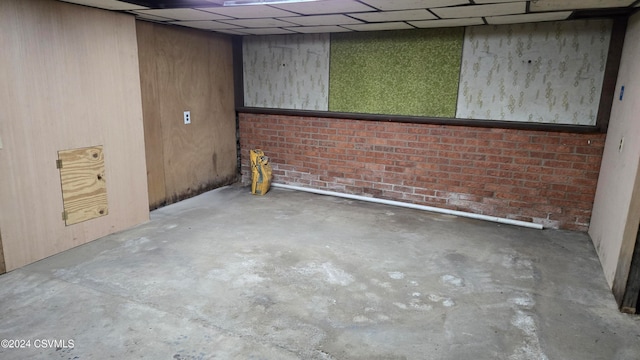 basement with a paneled ceiling, brick wall, wooden walls, and bar