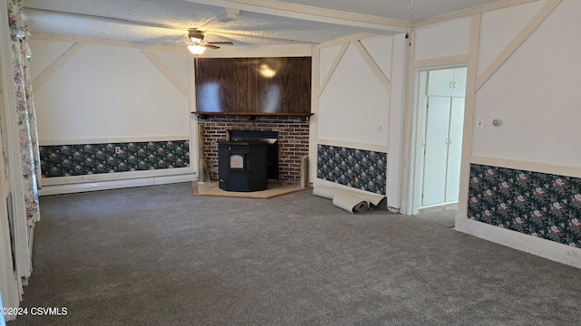 unfurnished living room with a textured ceiling, ceiling fan, a wood stove, and dark colored carpet