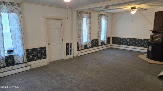 unfurnished living room with ceiling fan, crown molding, a wood stove, baseboard heating, and dark carpet