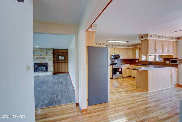 kitchen with sink, light brown cabinetry, light hardwood / wood-style floors, kitchen peninsula, and stainless steel appliances