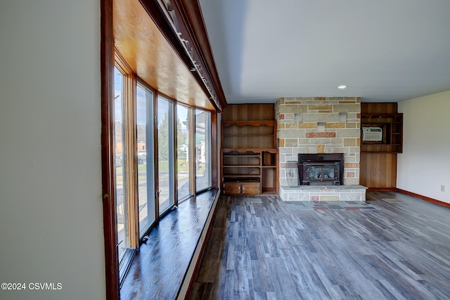 unfurnished living room featuring a stone fireplace, an AC wall unit, dark wood-type flooring, and wooden walls