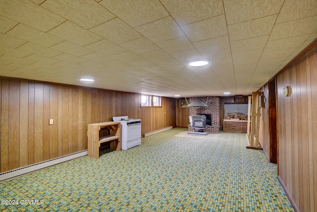 basement featuring wood walls, a wood stove, and a baseboard radiator