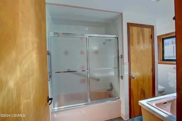 full bathroom featuring shower / bath combination with glass door, sink, tile walls, and toilet