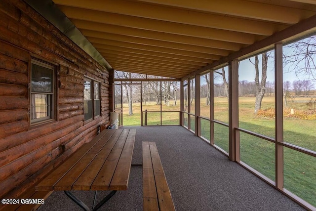 unfurnished sunroom featuring vaulted ceiling with beams and a healthy amount of sunlight