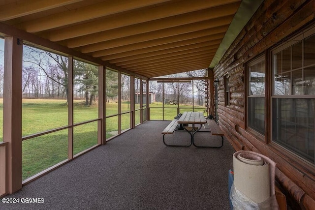 unfurnished sunroom featuring lofted ceiling with beams and a wealth of natural light