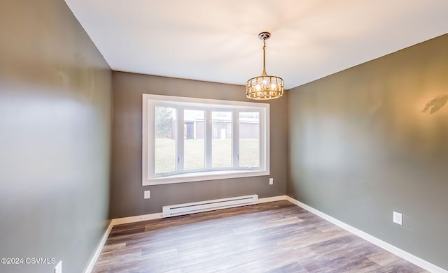 empty room with baseboard heating, a chandelier, and light hardwood / wood-style floors