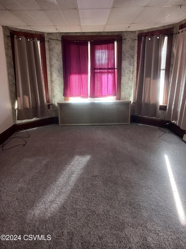 empty room featuring a paneled ceiling, carpet flooring, and radiator