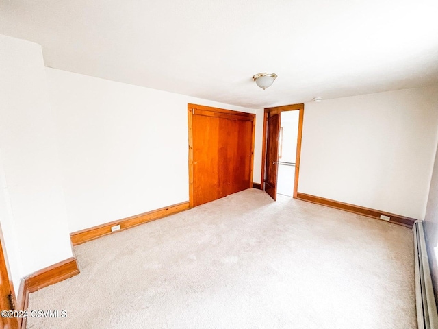 unfurnished bedroom with light colored carpet and a baseboard heating unit