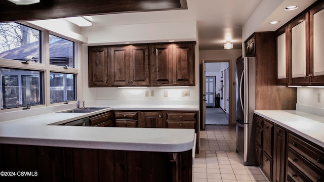 kitchen with kitchen peninsula, dark brown cabinets, sink, light tile patterned floors, and stainless steel refrigerator