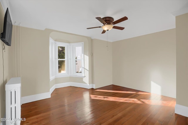 empty room with dark hardwood / wood-style floors, ceiling fan, and radiator