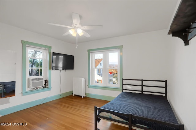 bedroom featuring multiple windows, ceiling fan, radiator heating unit, and hardwood / wood-style flooring