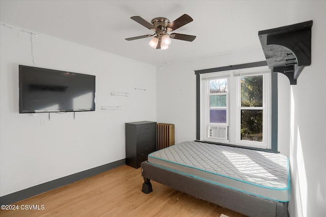 bedroom featuring ceiling fan, radiator heating unit, cooling unit, and wood-type flooring