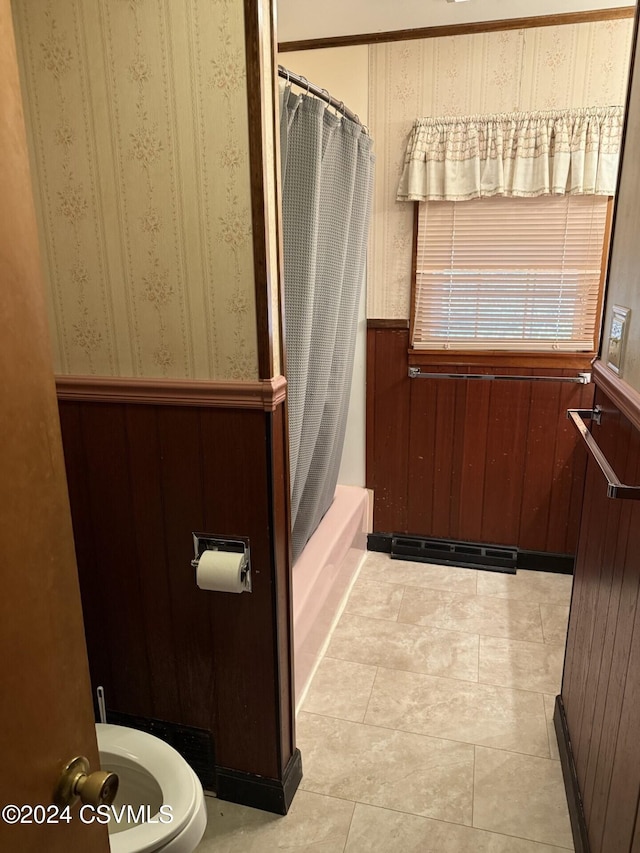 bathroom with wooden walls, tile patterned flooring, shower / tub combo, and toilet