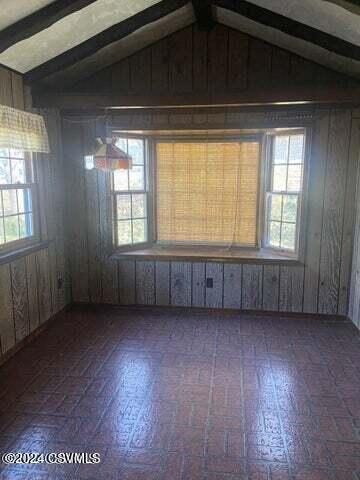 unfurnished room featuring wooden walls and lofted ceiling