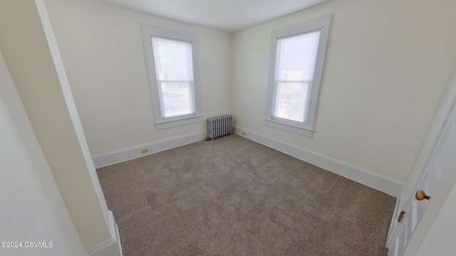 empty room with a wealth of natural light, light colored carpet, and radiator