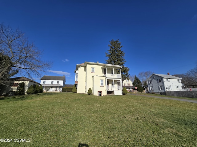 rear view of house featuring a balcony and a yard