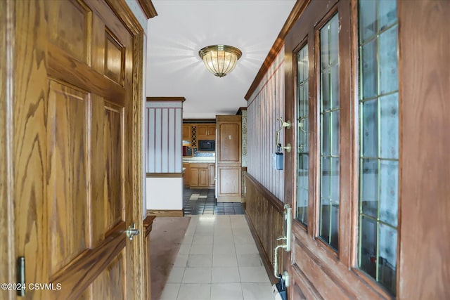 hall featuring wooden walls, crown molding, and light tile patterned floors