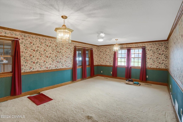 carpeted empty room featuring a textured ceiling, crown molding, and a chandelier