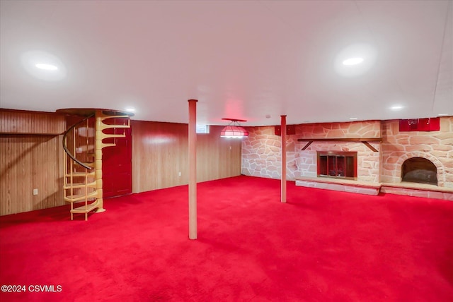 basement with carpet flooring, a stone fireplace, and wood walls