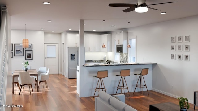 kitchen featuring light hardwood / wood-style flooring, kitchen peninsula, pendant lighting, white cabinets, and appliances with stainless steel finishes