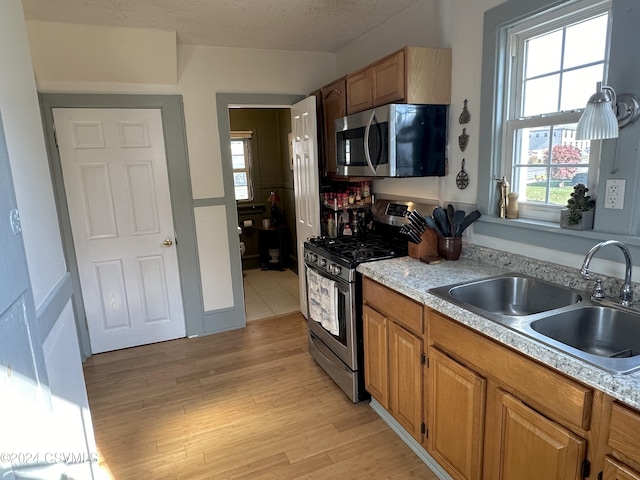 kitchen with appliances with stainless steel finishes, a textured ceiling, light hardwood / wood-style flooring, and sink