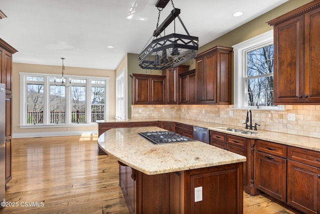 kitchen with an inviting chandelier, light wood-type flooring, light stone counters, a sink, and stainless steel appliances