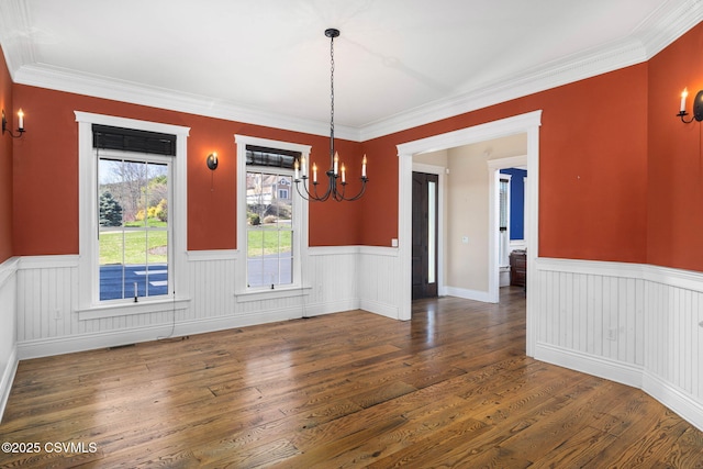 unfurnished dining area featuring wood finished floors, a notable chandelier, and a wainscoted wall