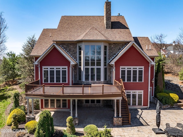 rear view of property featuring a chimney, a patio area, stone siding, and a deck
