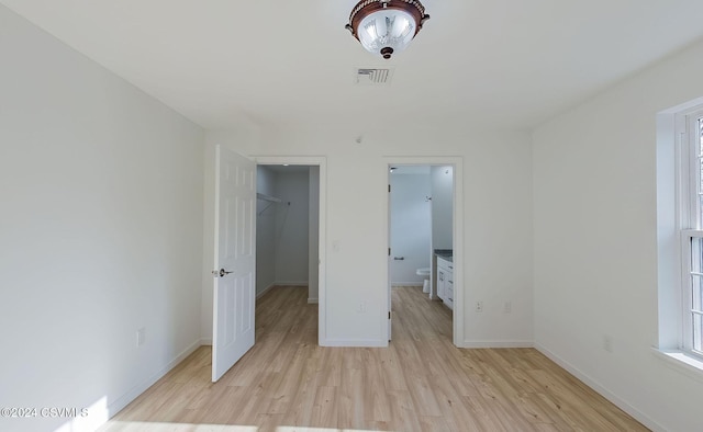 unfurnished bedroom featuring a walk in closet, light wood-type flooring, a closet, and connected bathroom