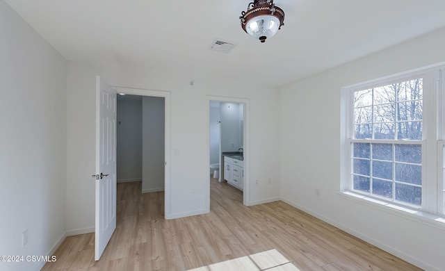 unfurnished bedroom with connected bathroom, a walk in closet, and light hardwood / wood-style flooring