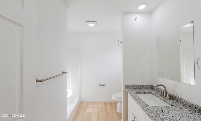 bathroom with hardwood / wood-style flooring, vanity, toilet, and a tub