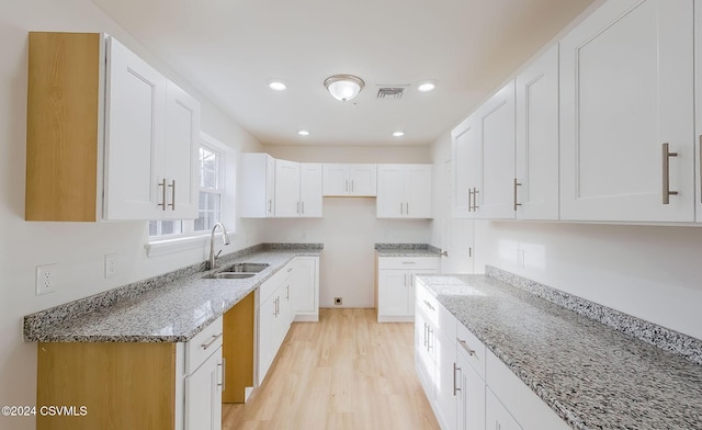 kitchen with white cabinets, light hardwood / wood-style floors, light stone countertops, and sink