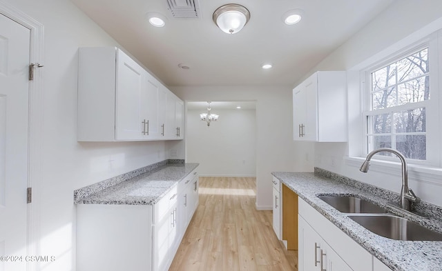 kitchen featuring white cabinets, light hardwood / wood-style floors, light stone countertops, and sink