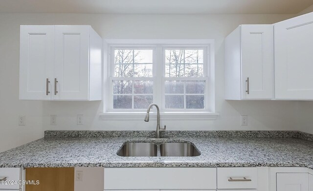 kitchen with white cabinets, light stone counters, and sink