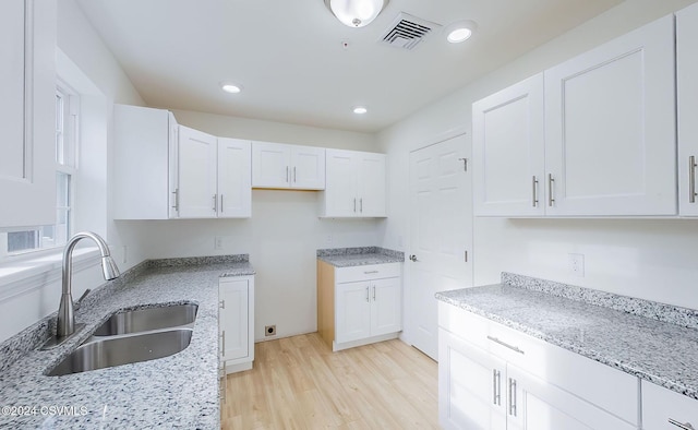 kitchen with light stone counters, sink, white cabinets, and light wood-type flooring