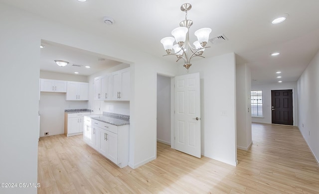 kitchen featuring an inviting chandelier, white cabinets, light hardwood / wood-style flooring, light stone countertops, and decorative light fixtures