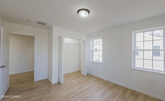 unfurnished bedroom with a closet, light hardwood / wood-style flooring, and multiple windows