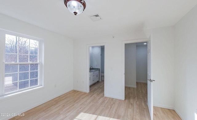 unfurnished bedroom featuring ensuite bath and light hardwood / wood-style floors