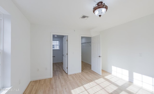 unfurnished bedroom featuring a walk in closet, a closet, and light hardwood / wood-style floors