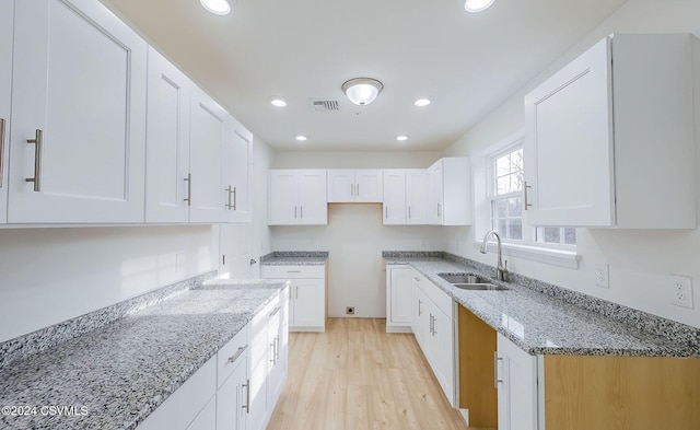 kitchen with light stone counters, light hardwood / wood-style flooring, white cabinetry, and sink